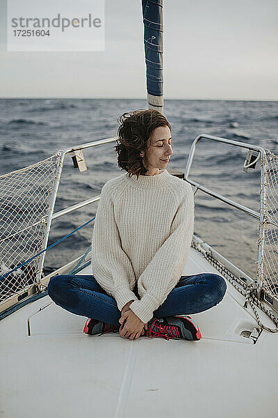 Frau mit geschlossenen Augen auf einem Boot im Meer sitzend im Urlaub