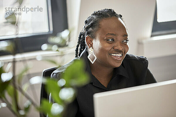 Lächelnde Unternehmerin  die wegschaut  während sie im Büro sitzt