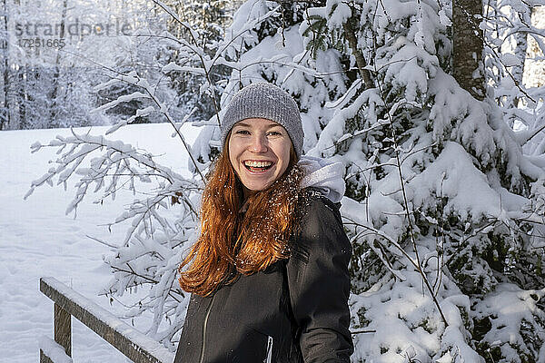 Glückliche Frau mit roten Haaren vor einem schneebedeckten Baum im Winter