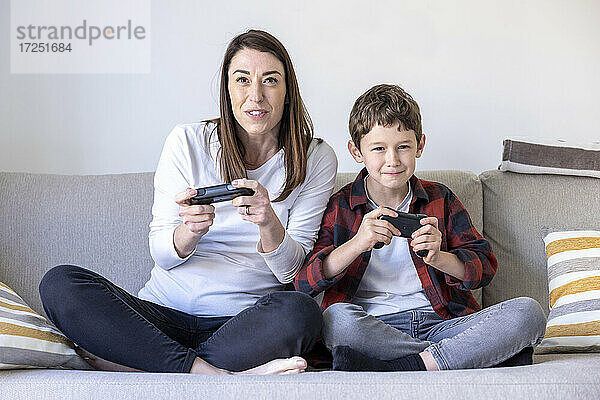 Aufgeregte Frau und Sohn spielen ein Videospiel  während sie auf dem Sofa im Wohnzimmer sitzen