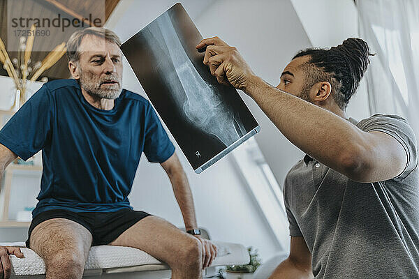Physiotherapeut bespricht Röntgenbild eines Knies mit einem männlichen Patienten
