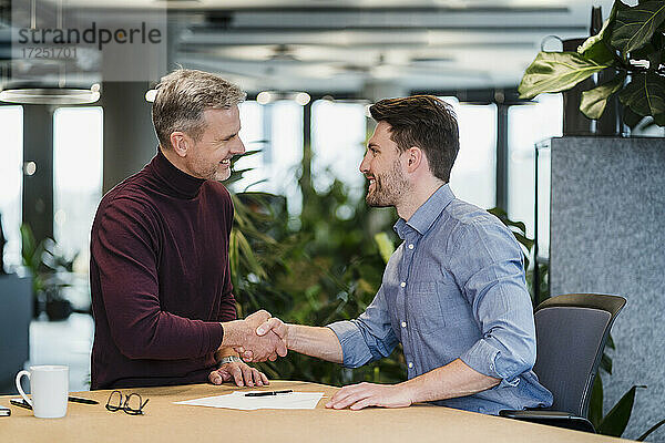 Lächelnde Geschäftsleute beim Händeschütteln am Arbeitsplatz