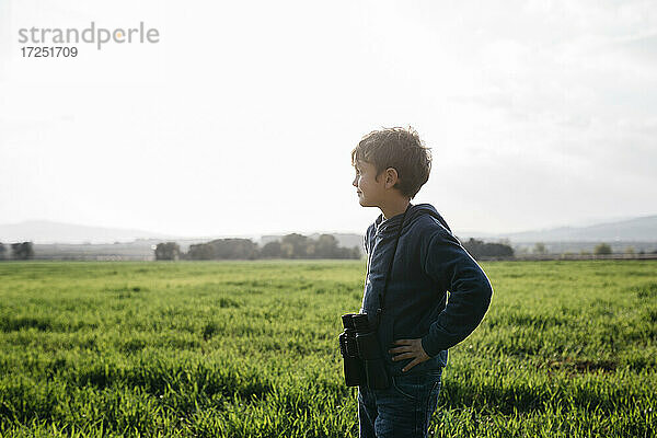 Niedlicher Junge mit Fernglas schaut weg  während er in einem Feld an einem sonnigen Tag steht