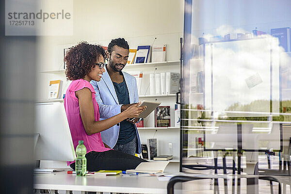 Männliche und weibliche Berufstätige planen im Büro über ein digitales Tablet  durch Glas gesehen