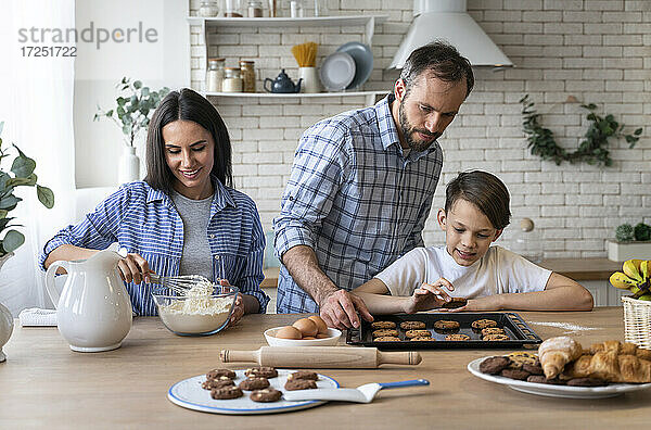 Vater und Sohn betrachten einen Keks  während die Mutter in der Küche zu Hause Mehl mischt