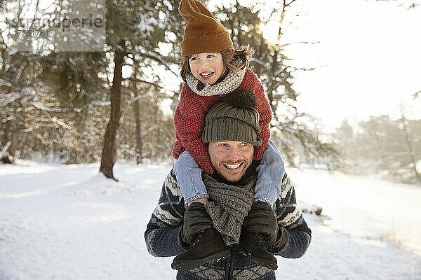 Lächelnder Vater schaut weg  während er seinen Sohn im Winter auf der Schulter trägt