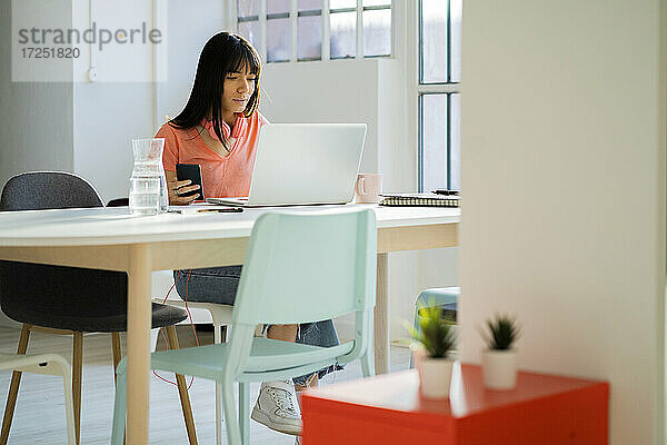 Geschäftsfrau mit Smartphone und Laptop im Heimbüro