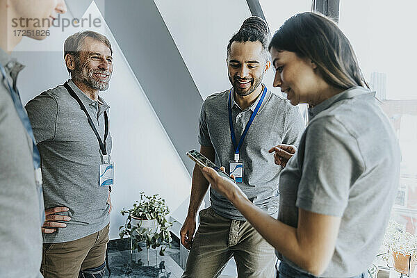 Lächelnde weibliche Fachkraft  die mit einem männlichen Kollegen während einer Konferenz über ein Mobiltelefon diskutiert