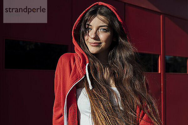 Lächelndes Teenager-Mädchen in roter Kapuzenjacke an einem sonnigen Tag