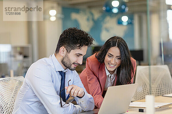 Lächelnde männliche und weibliche Fachleute  die über einem Laptop in einem Coworking-Büro diskutieren