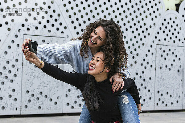 Glückliche junge Freundinnen nehmen Selfie durch Smartphone vor der Wand