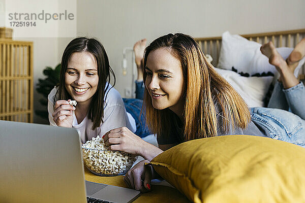 Lächelnde Freunde  die Popcorn genießen  während sie einen Film im Schlafzimmer ansehen