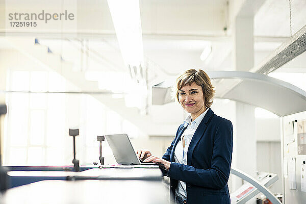 Lächelnde Geschäftsfrau vor einem Laptop in einer Druckwerkstatt