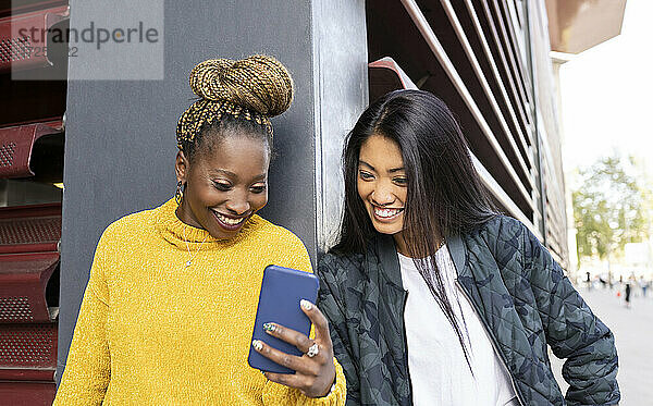 Multiethnische Freundinnen schauen auf ihr Smartphone an der Wand