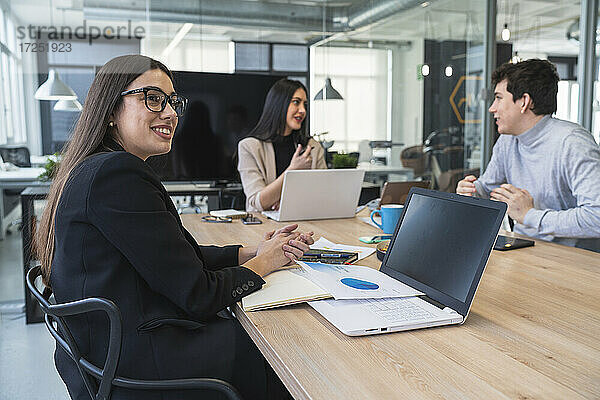 Geschäftsfrau schaut weg  während ein männlicher und ein weiblicher Kollege am Konferenztisch im Büro diskutieren