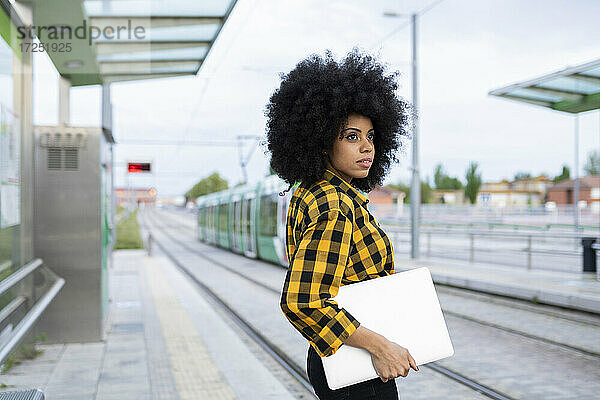 Junge Frau schaut weg und hält einen Laptop am Bahnhof