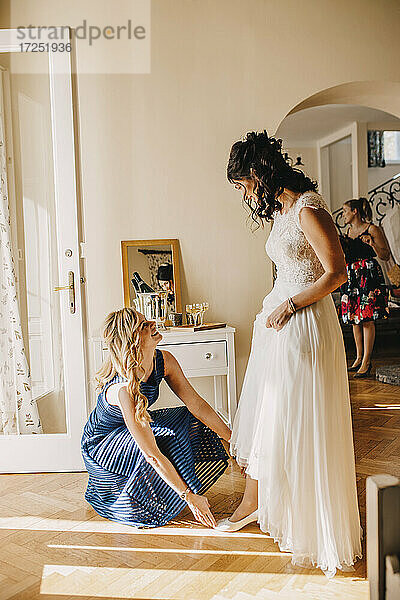 Lächelnde Brautjungfer hilft der Braut beim Anziehen des Schuhs