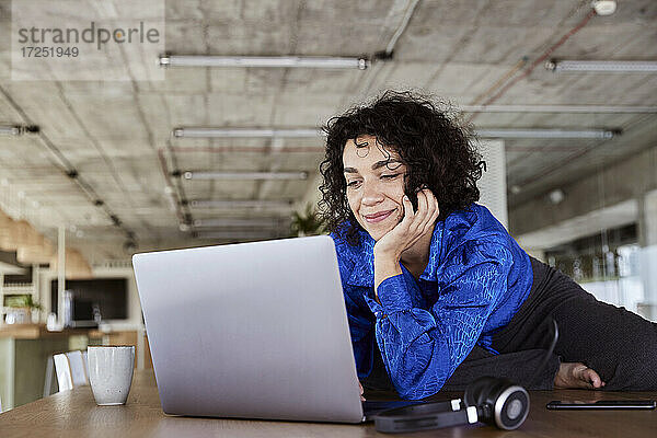 Lächelnde Frau mit Laptop auf dem Tisch im Loft