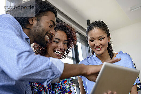 Lächelnde junge Kollegen  die ein digitales Tablet in der Universität benutzen