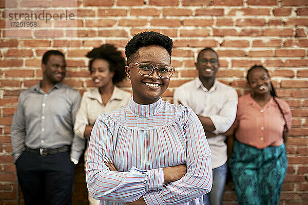 Lächelnde Geschäftsfrau mit Brille  im Hintergrund stehen Kollegen im Büro