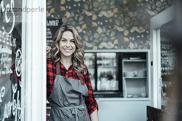 Weibliche Unternehmerin lächelt  während sie vor der Tür eines Cafés steht