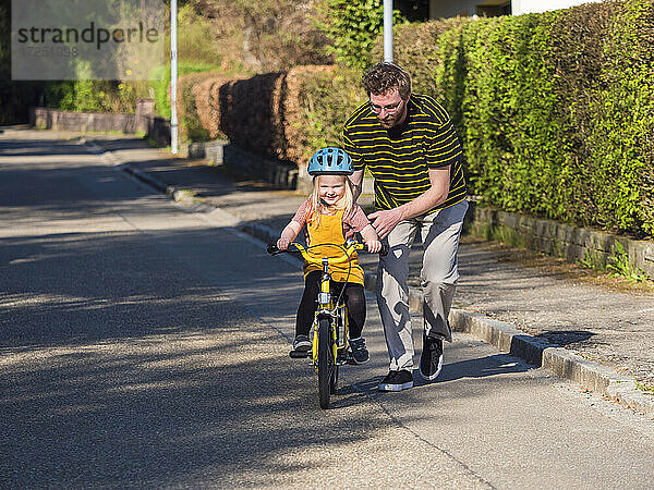 Vater bringt seiner Tochter in der Nähe des Gehwegs auf der Straße das Radfahren bei