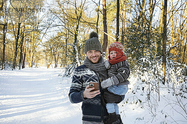 Vater trägt seinen Sohn und hält dabei sein Smartphone im Winter