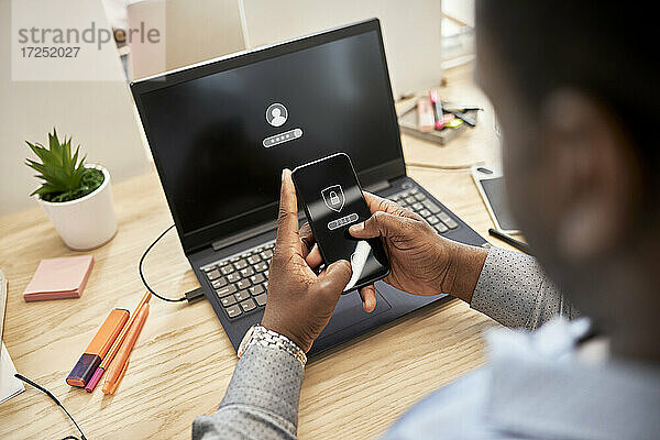 Geschäftsmann schützt Daten  während er im Büro ein Smartphone über einem Laptop benutzt
