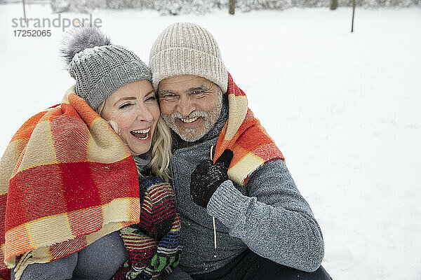 Lächelndes  in eine Decke eingewickeltes Paar im Winter