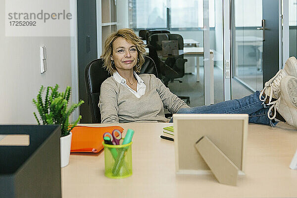 Weibliche Fachkraft mit hochgelegten Füßen  die wegschaut  während sie am Schreibtisch im Büro sitzt