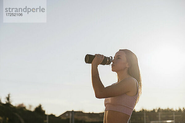 Weibliche Athletin trinkt an einem sonnigen Tag Wasser aus einer Flasche