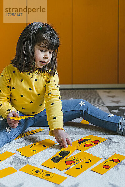 Mädchen spielt mit Emoticons  während sie zu Hause auf dem Boden sitzt