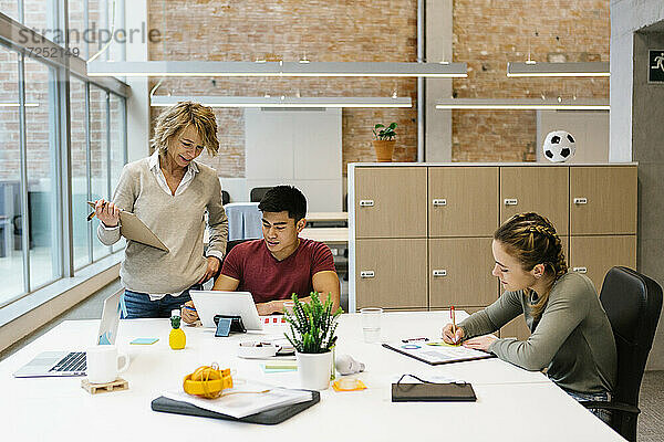 Eine Unternehmerin unterstützt einen jungen männlichen Mitarbeiter bei einer Besprechung im Büro