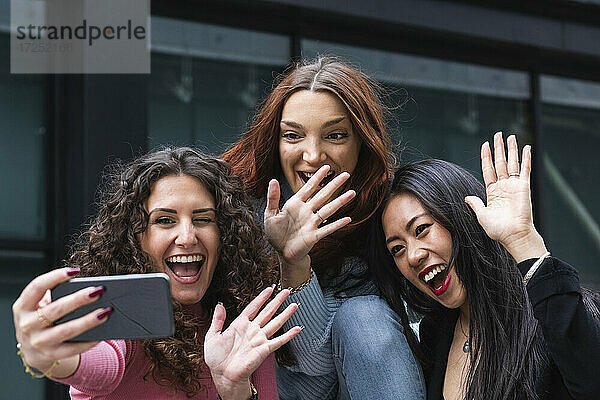 Fröhliche Freunde winken mit der Hand zum Videoanruf auf dem Handy