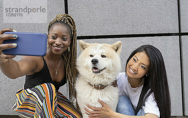 Weibliche Freunde nehmen Selfie mit Akita Hund durch Smartphone von der Wand