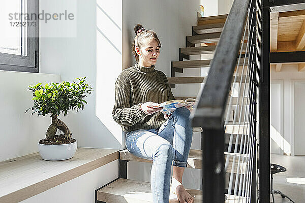 Frau liest Buch auf der Treppe zu Hause an einem sonnigen Tag