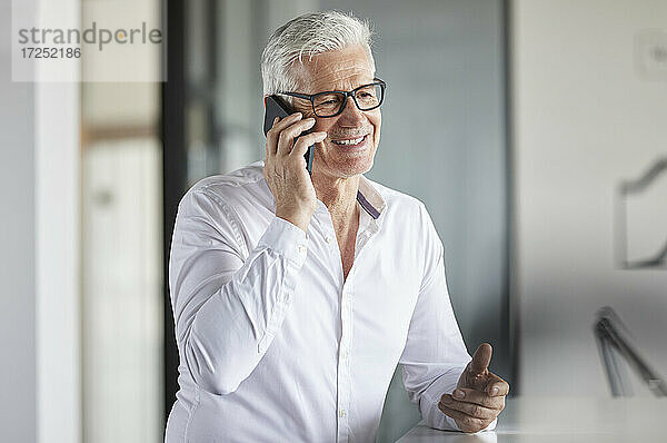 Männlicher Unternehmer mit Brille  der im Büro mit einem Mobiltelefon spricht