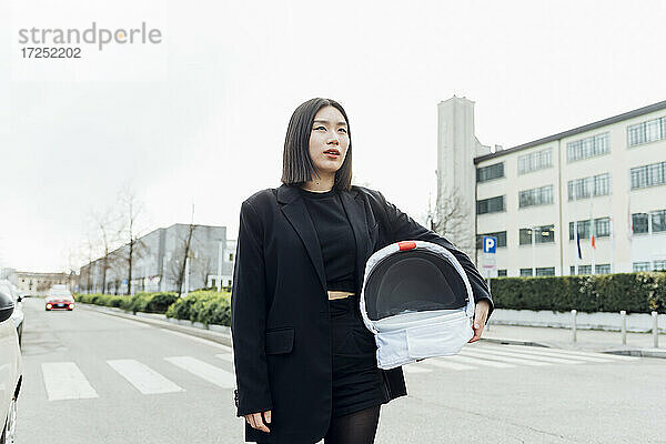 Junge Frau mit Weltraumhelm auf der Straße in der Stadt stehend