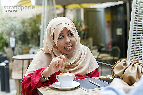 Lächelnde junge Frau  die in einem Straßencafé Kaffee umrührt