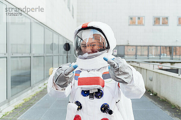 Junge Astronautin zeigt den Mittelfinger  während sie in der Nähe eines Gebäudes steht