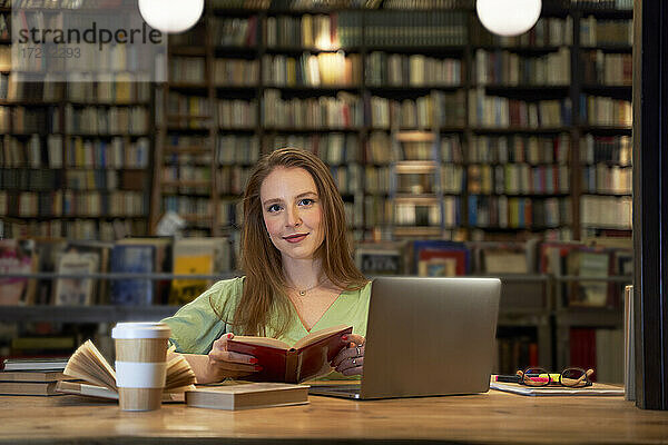 Lächelnde Frau mit Buch in der Bibliothek