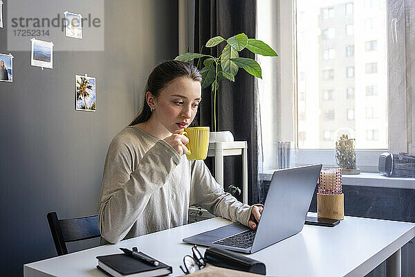 Frau trinkt Kaffee bei der Arbeit am Laptop im Büro zu Hause