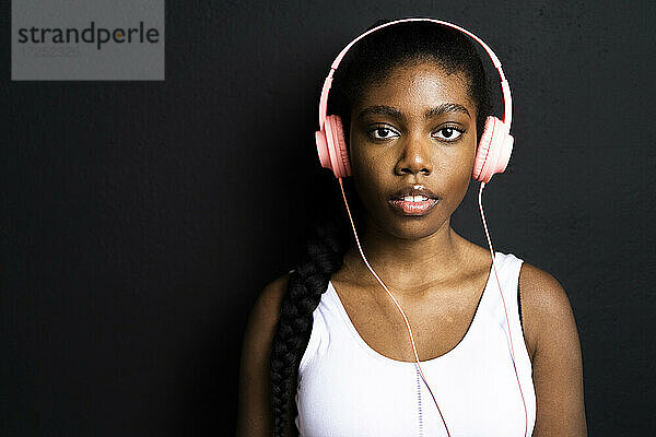 Schöne Frau hört Musik über Kopfhörer vor schwarzem Hintergrund