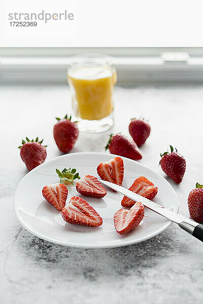 Glas Orangensaft  Küchenmesser und Teller mit frischen Erdbeeren liegen auf weißem Marmor
