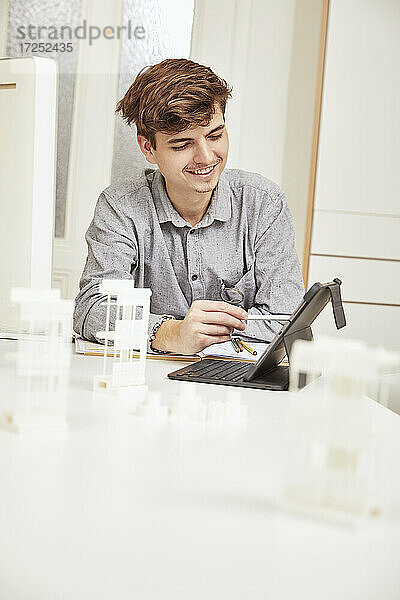 Lächelnder männlicher Architekt  der im Büro sitzend an einem digitalen Tablet arbeitet