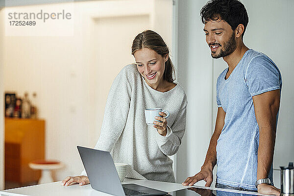 Glückliche Frau schaut auf einen Laptop  während sie bei ihrem Freund zu Hause steht