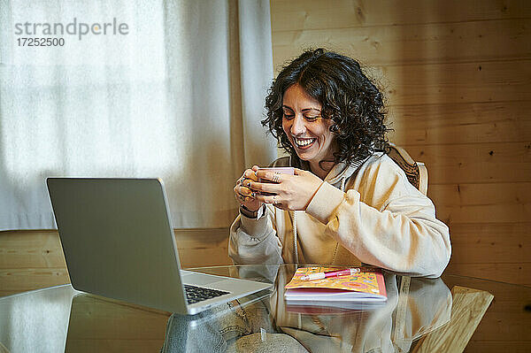 Glückliche Frau beim Tee vor dem Laptop zu Hause