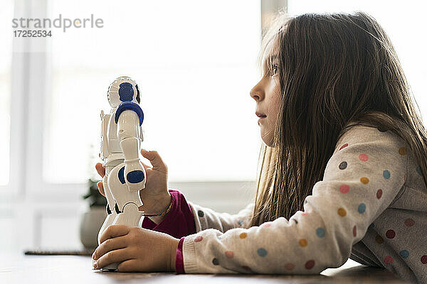 Nachdenkliches Mädchen  das wegschaut  während es ein Roboterspielzeug zu Hause hält