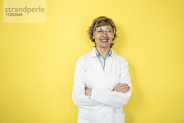Weibliche Fachkraft in Arbeitsschutzkleidung vor einer gelben Wand stehend