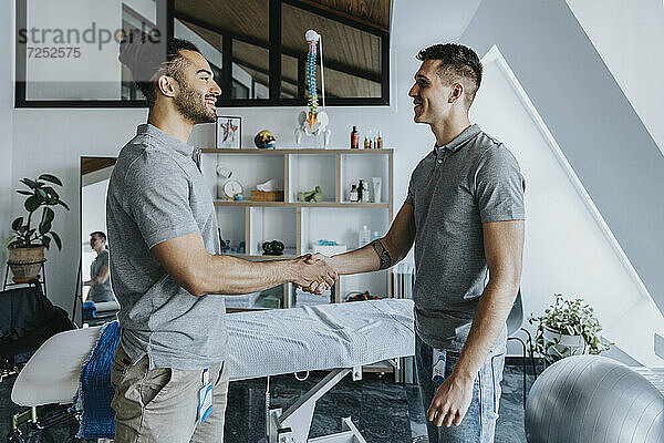 Männliche Physiotherapeuten lächeln beim Händeschütteln in der Praxis